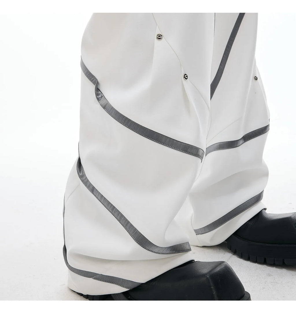 Men's black trousers with pleated detail and metal rivets, showing three-dimensional cut.