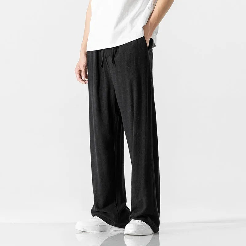Man wearing beige straight-leg cropped bamboo fibre trousers with a drawstring waist on a summer day.