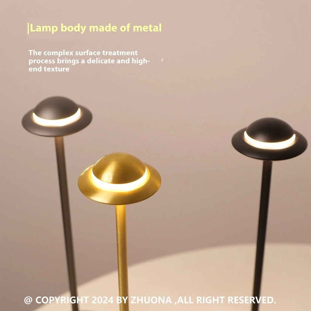 Modern metallic UFO-shaped table lamp with touch base in black, on a wooden desk.