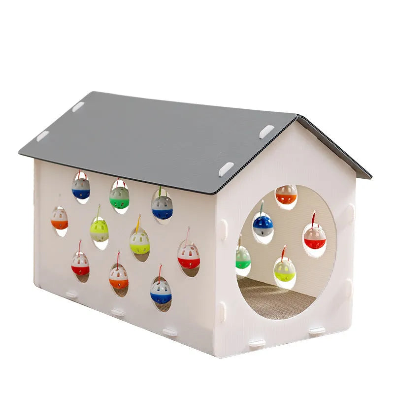 White plastic house-shaped cat scratch board with sisal siding, an arched tunnel entrance, and a dangling red bell ball toy.