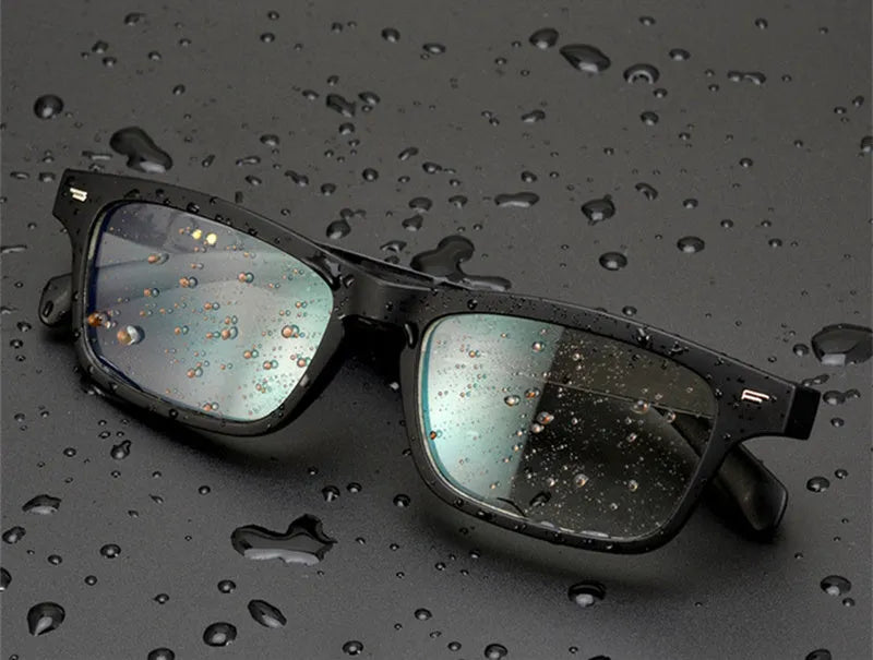Smart Bluetooth audio glasses with dark lenses on a table, showing temple speakers and a charging case.