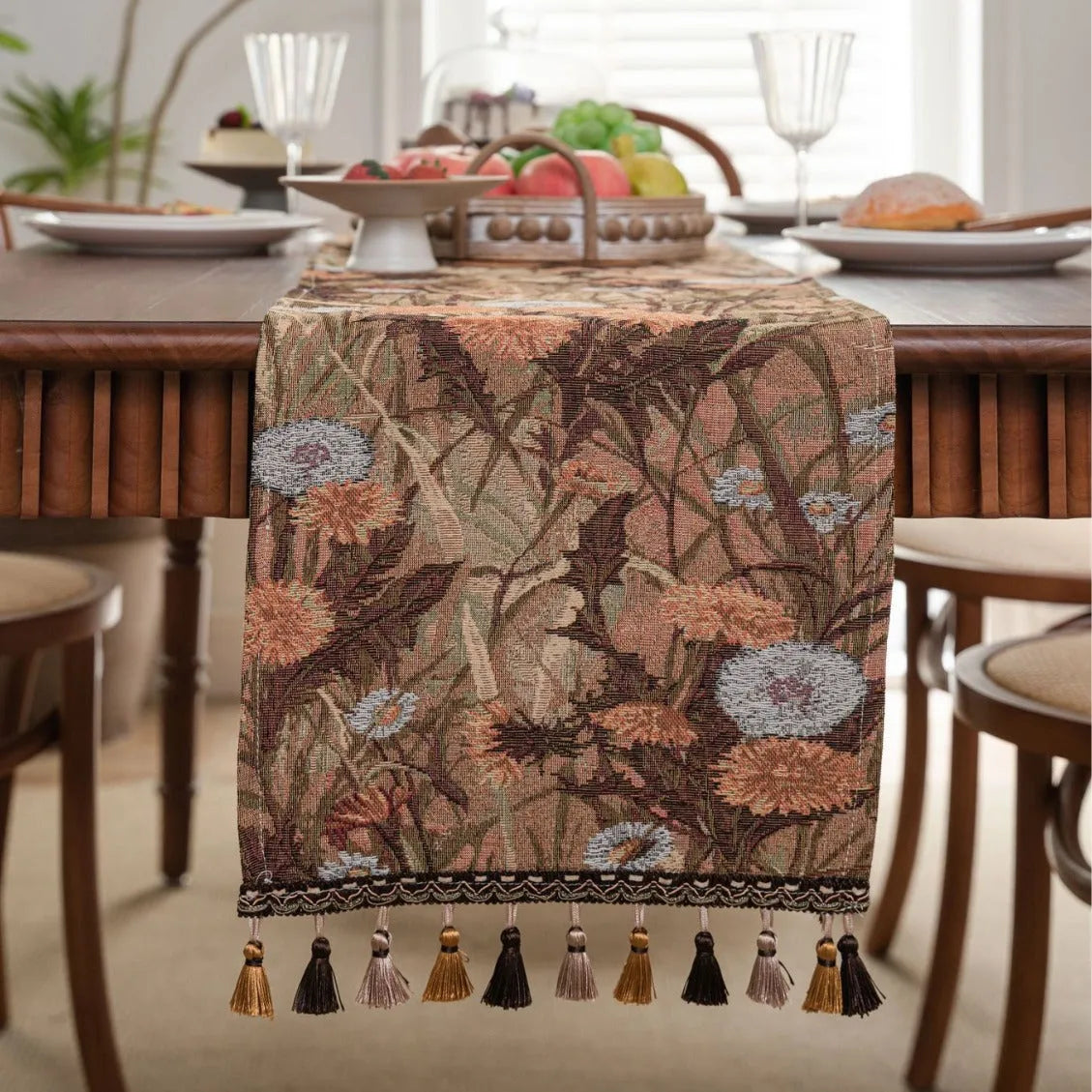 Beige jacquard table runner with floral pattern and long tassels on a wooden dining table.