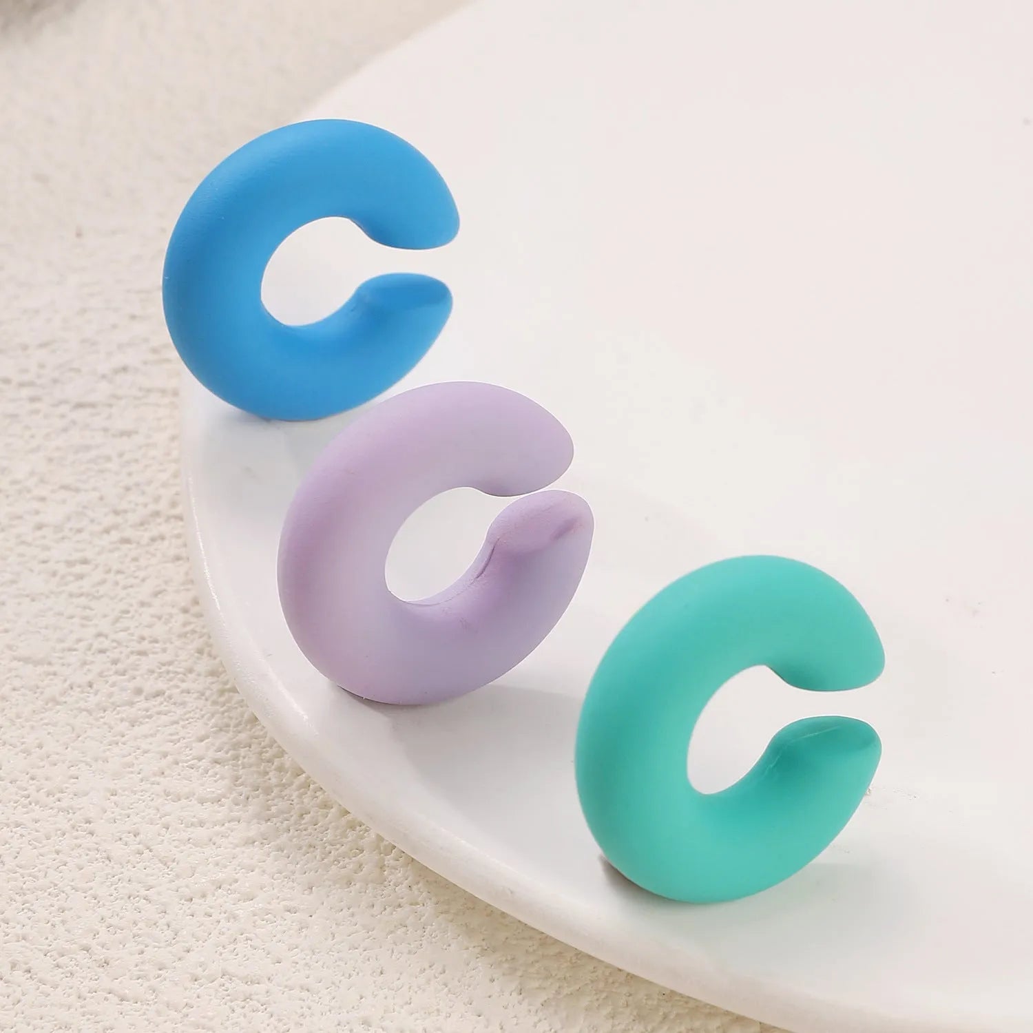Close-up of a pair of matte coarse round C-shaped clip-on earrings for women in a candy colour.