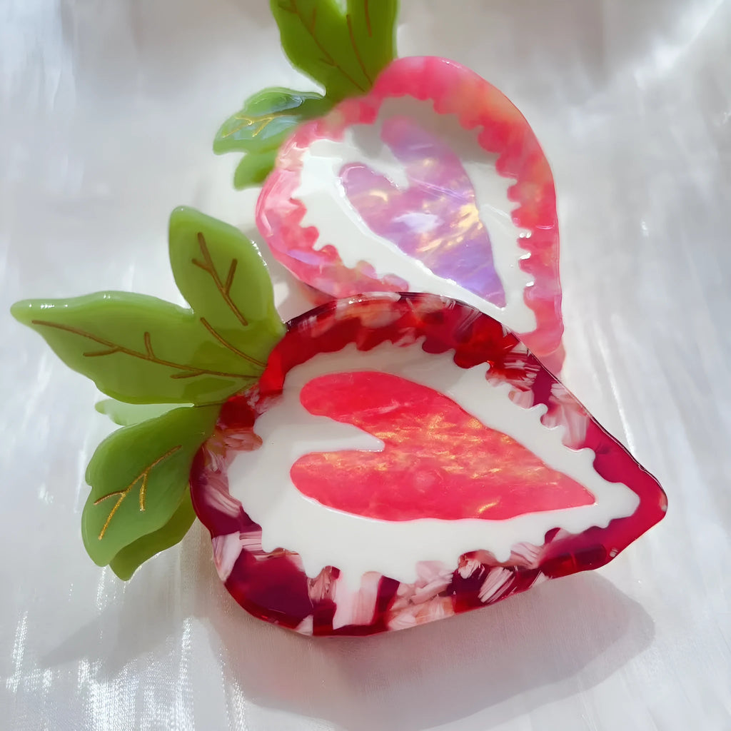Red and pink strawberry-shaped metal charm hair clip for girls on a white background.