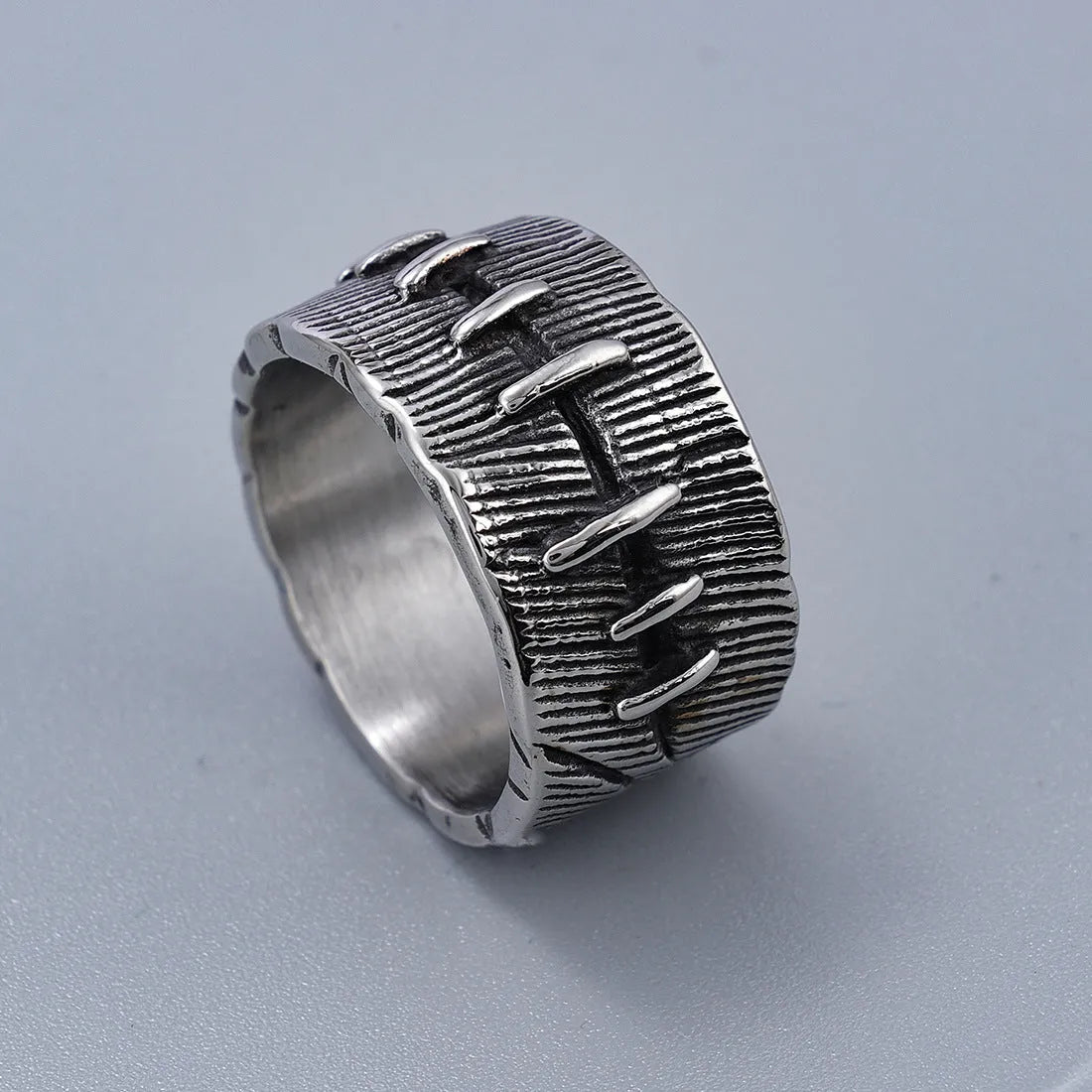 A dark geometric titanium steel ring with punk stitching and a double ring design on a grey background.