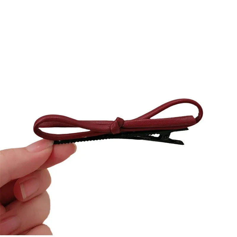Wine red genuine leather bow hair clip on a dark background, showing metal clasp.