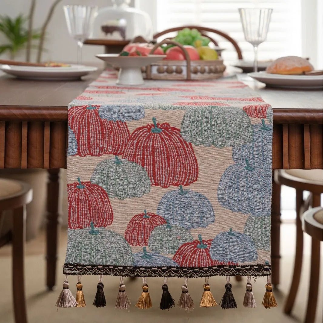 Beige jacquard table runner with floral pattern and long tassels on a wooden dining table.