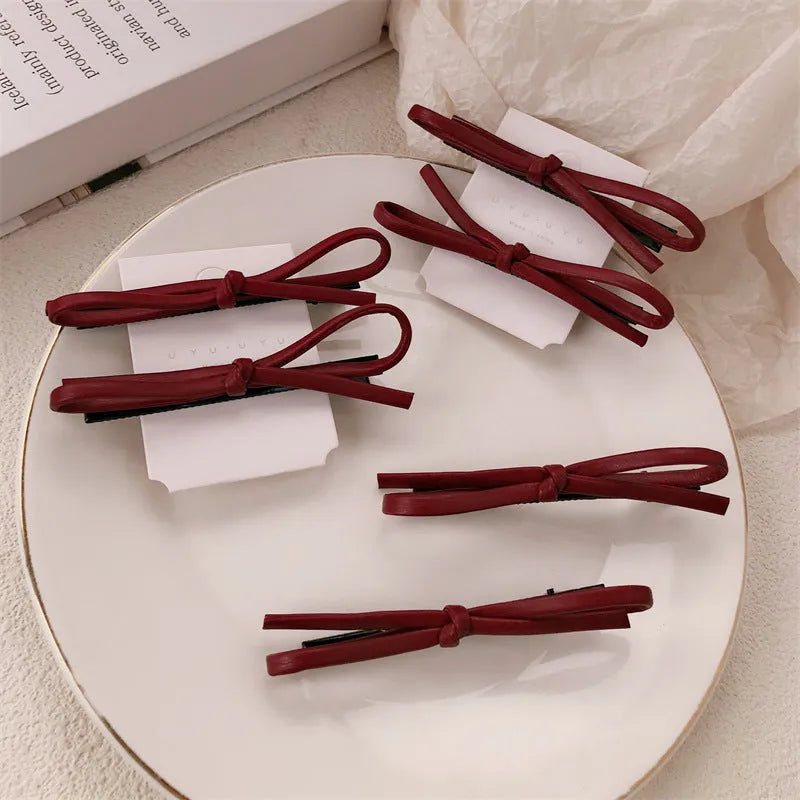 Wine red genuine leather bow hair clip on a dark background, showing metal clasp.