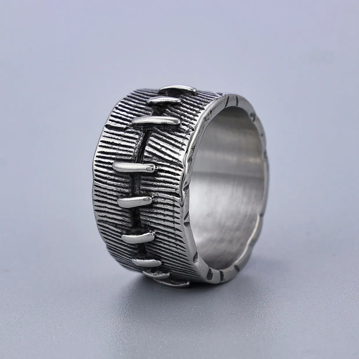 A dark geometric titanium steel ring with punk stitching and a double ring design on a grey background.