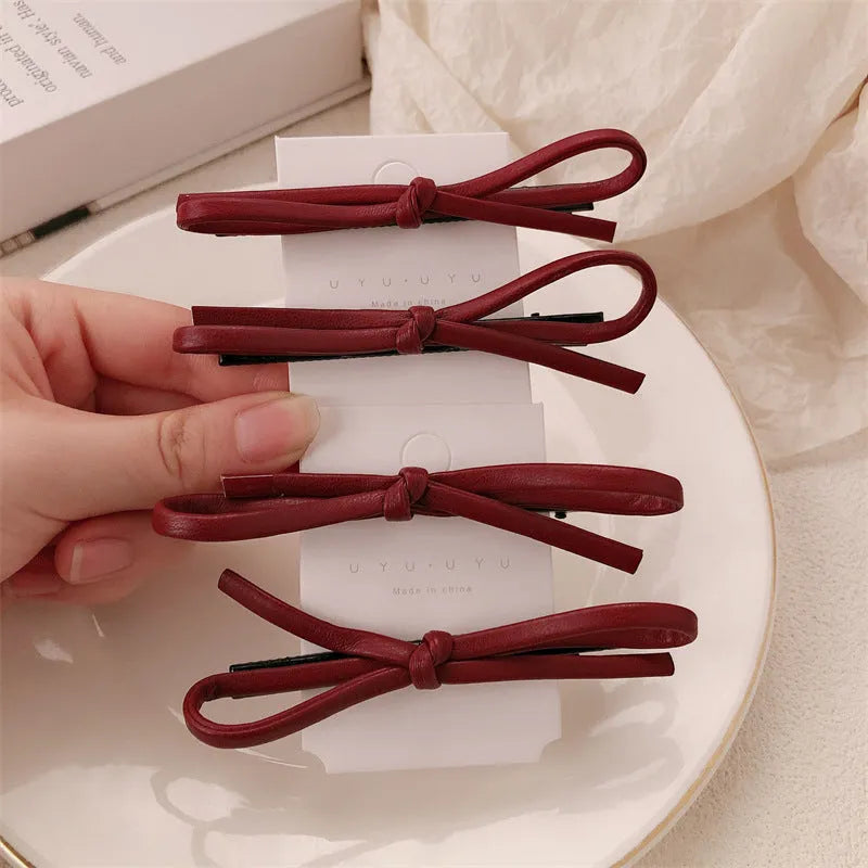 Wine red genuine leather bow hair clip on a dark background, showing metal clasp.
