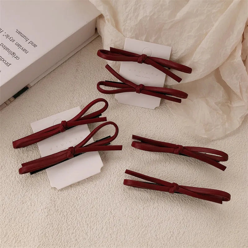 Wine red genuine leather bow hair clip on a dark background, showing metal clasp.