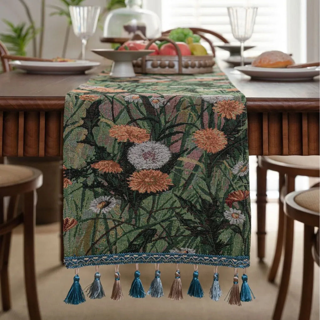 Beige jacquard table runner with floral pattern and long tassels on a wooden dining table.