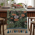 Beige jacquard table runner with floral pattern and long tassels on a wooden dining table.