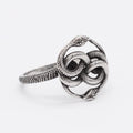 Close-up of a steel-coloured titanium steel ring featuring a detailed double snake design on a dark background.
