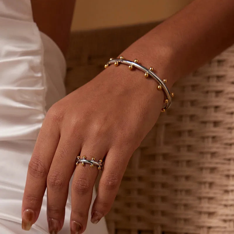 Stainless steel C-shaped bracelet with textured bean beads and rivet details in gold, steel colour, or steel colour gold finishes