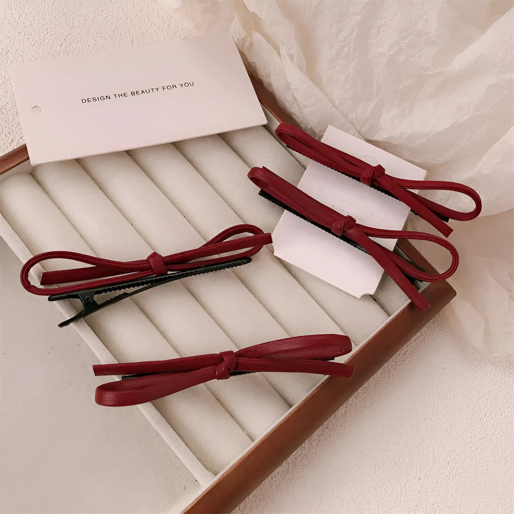 Wine red genuine leather bow hair clip on a dark background, showing metal clasp.