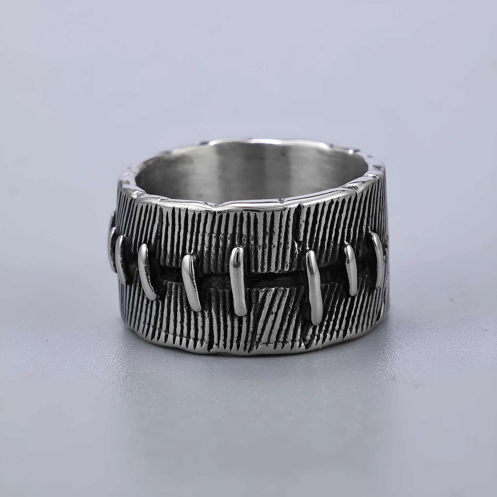 A dark geometric titanium steel ring with punk stitching and a double ring design on a grey background.