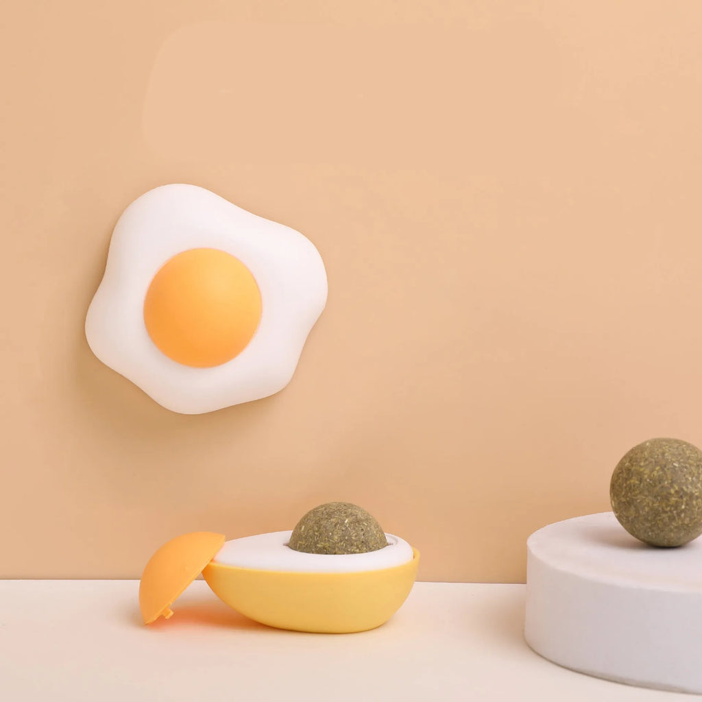Catnip ball toy with adhesive backing attached to wall, showing cat head shape design