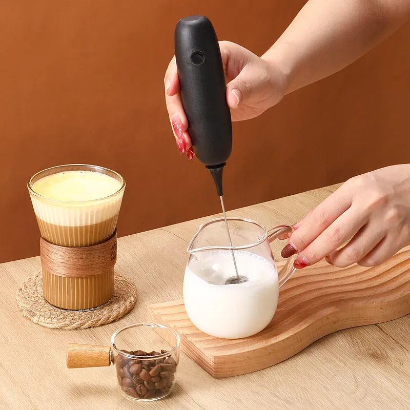 A handheld electric milk frother and blender in black and white colours on a kitchen counter.