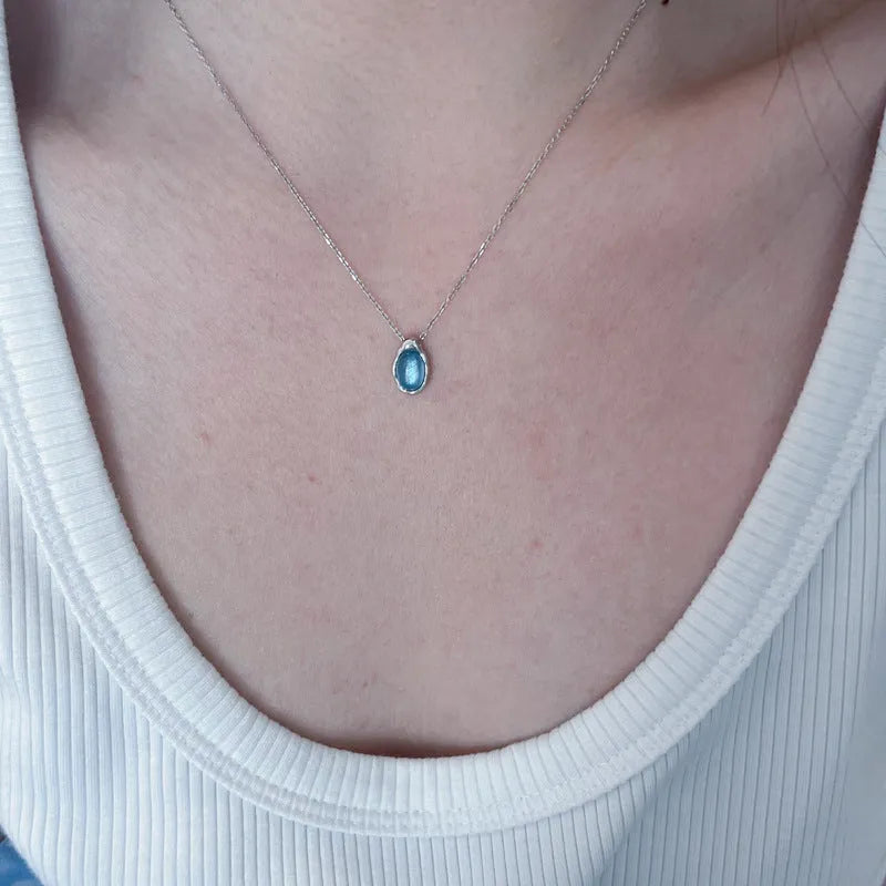 Navy blue water drop pendant necklace on a cross-chain, showing geometric shape and platinum colour accents.