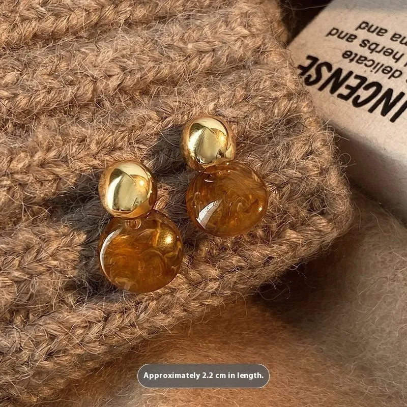 Set of three pairs of geometric holiday earrings: round studs, irregular amber studs, and tassel drop earrings.