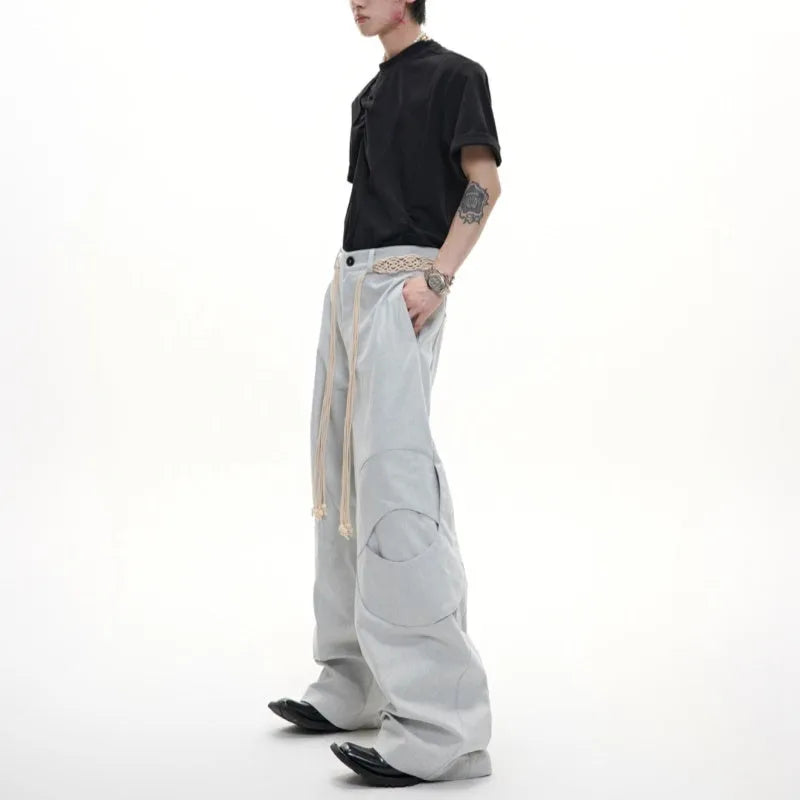 Man wearing dark blue cotton straight-leg trousers with heavy 3D belt stitching and decorative tassel details.