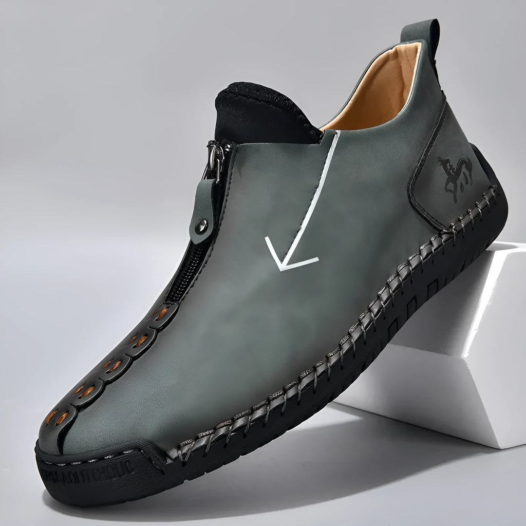 Men's black leather ankle boots with a front zip and hand-stitched detailing on a rubber sole.