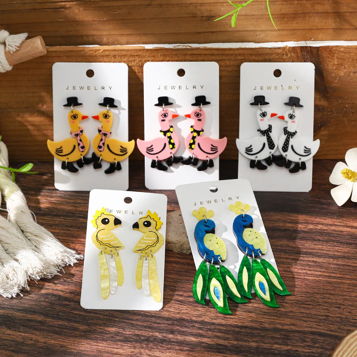 Three pairs of acrylic cartoon duck earrings in pink, white, and yellow on a light background