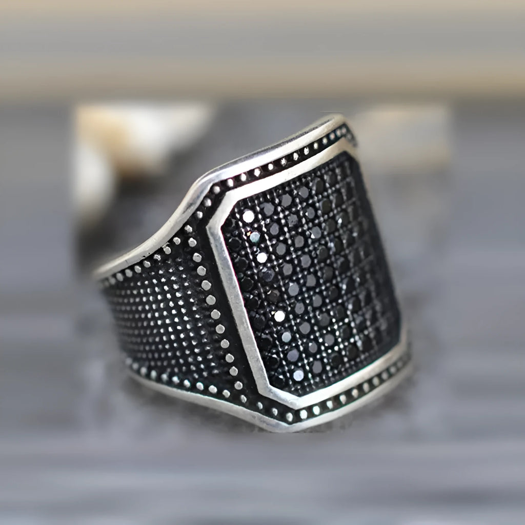 Close-up of a black alloy ring with a zircon stone set in a copper inlay pattern on a person's finger.
