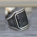 Close-up of a black alloy ring with a zircon stone set in a copper inlay pattern on a person's finger.