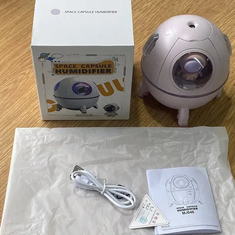 Light purple astronaut-shaped USB desktop humidifier with colourful LED light on a desk.