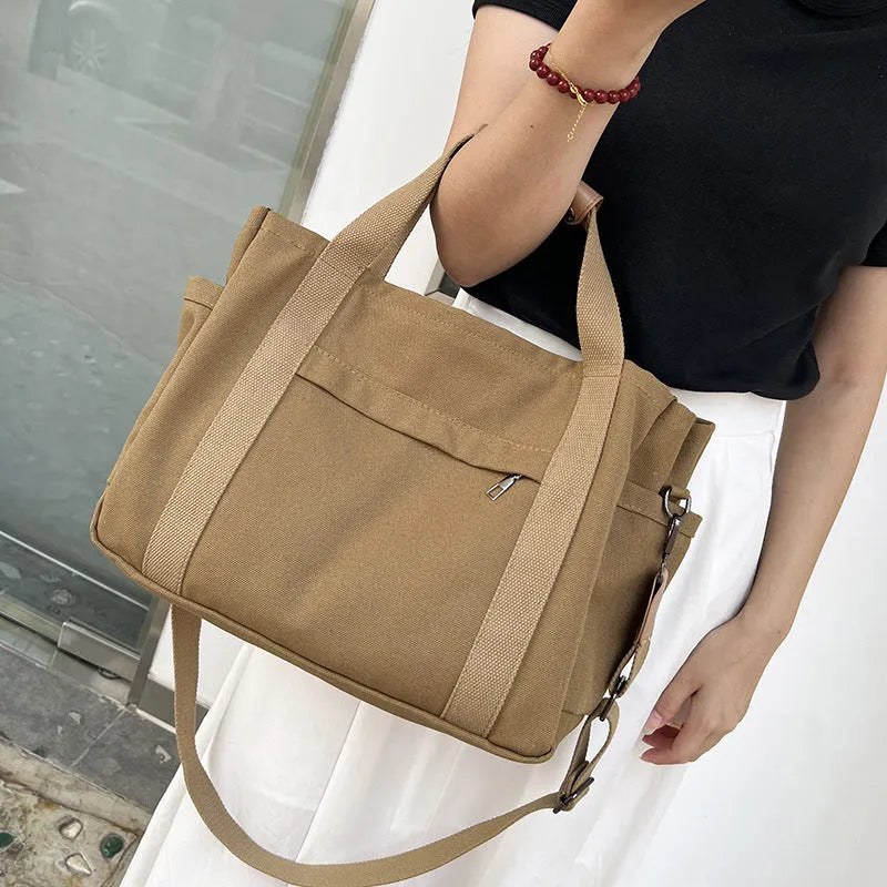 A horizontal square canvas tote bag in army green with a cross-body strap and visible sewing lines.