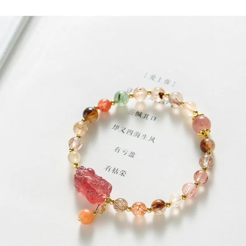 Close-up of a women's copper bracelet with a pink Strawberry Quartz crystal, a detailed Pixiu charm, and a white freshwater pearl.
