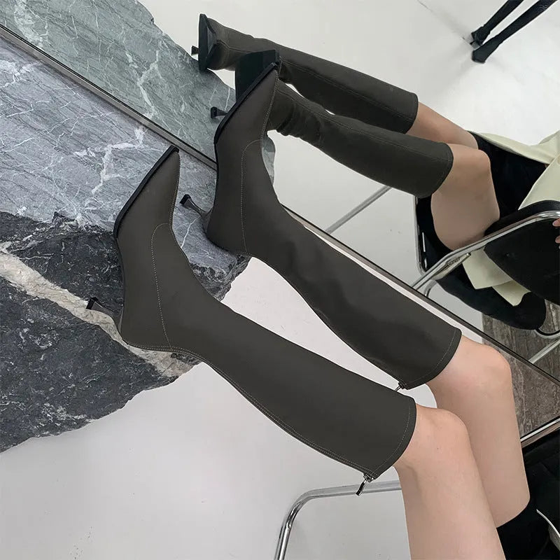 Women's black pointed toe knee-high boots with a stiletto heel and a back zip, shown on a foot.