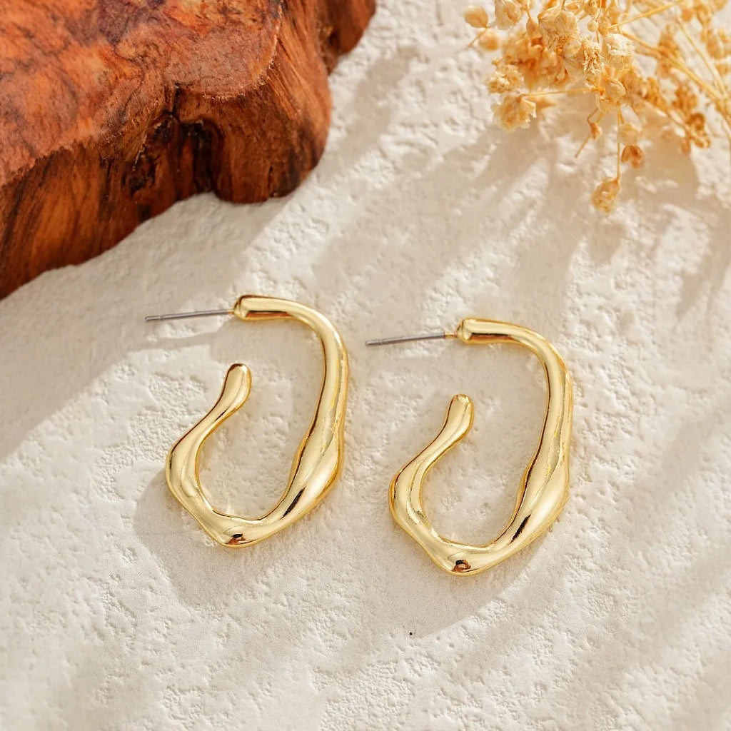 Gold irregular shaped minimalist earrings for women with a geometric silhouette on a plain background.