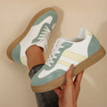 Green women's retro sports pumps with cross straps, leather stitching, and a round toe on a rubber sole.