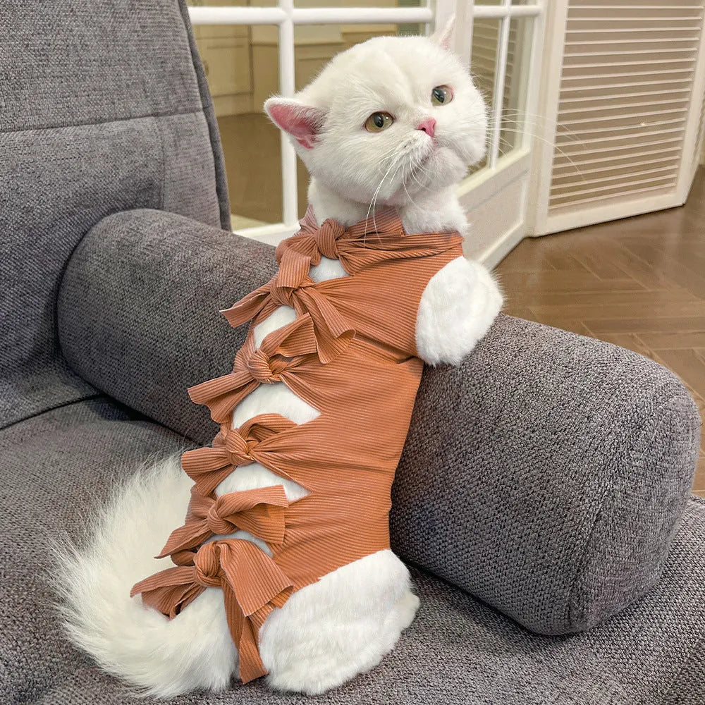 Pink lace-up cat recovery bodysuit on a table, showing back ties and full-body design for post-surgery care.