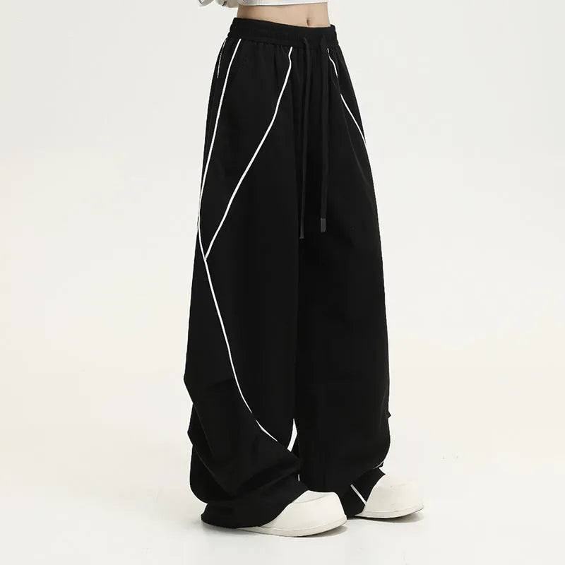 Black sports trousers with white stripes, showing wide-leg loose fit and mid-waist design.