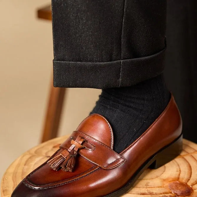 Men's black and brown polished leather tassel loafers for business casual wear, shown from the side.