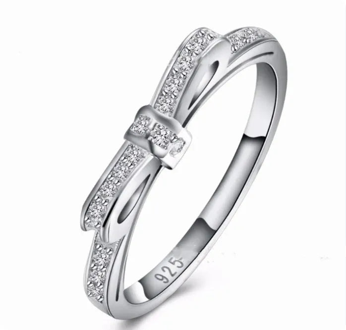 Silver coloured ring with a detailed bow shape set with clear sparkling zircon crystals on a model's hand.