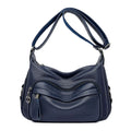 Blue horizontal square women's crossbody bag with a soft handle and zipper opening, showing organiser pockets inside.