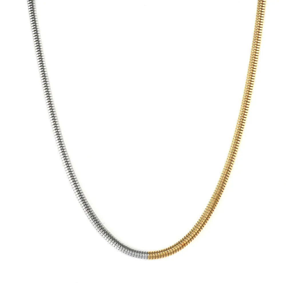 Close-up of a cold gold 3mm wide snake bone chain necklace with a geometric box clasp on a dark background.