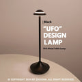 Modern metallic UFO-shaped table lamp with touch base in black, on a wooden desk.