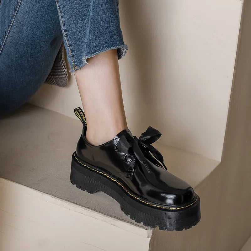 Women's black leather shoes with a thick sole, cross straps, and ribbon laces laid flat.