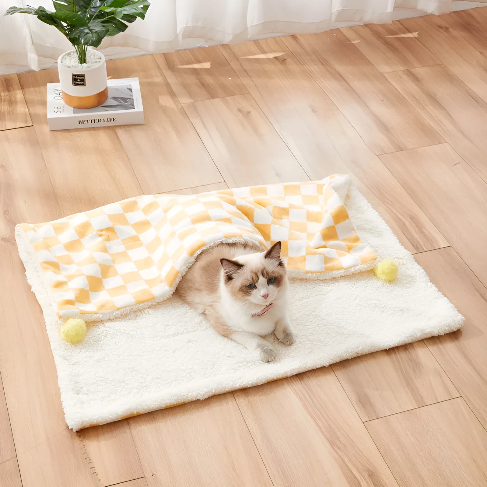 Green plaid pattern fleece pet blanket with a fur ball decoration, shown on a sofa.