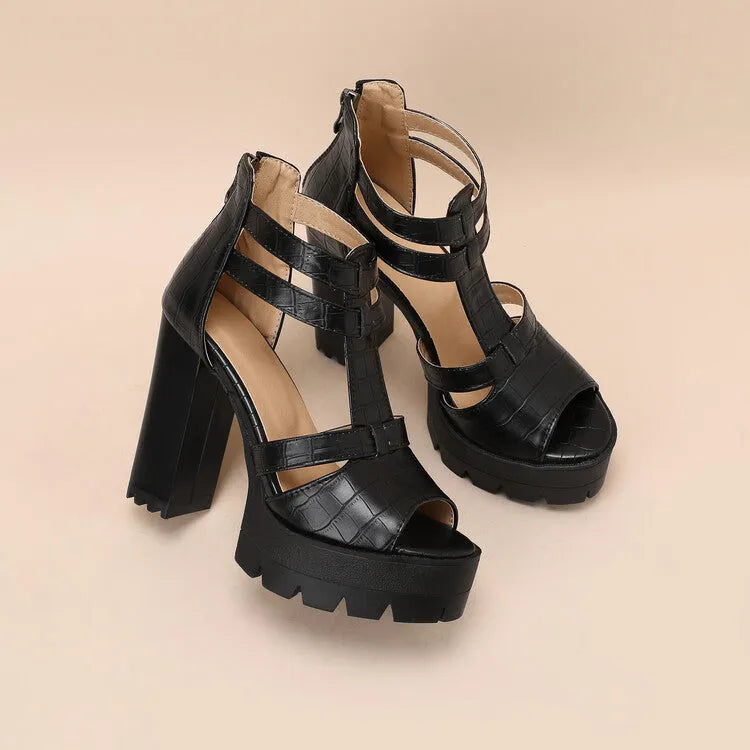 Black platform high heel sandals with a round toe and back zipper on a wooden floor.