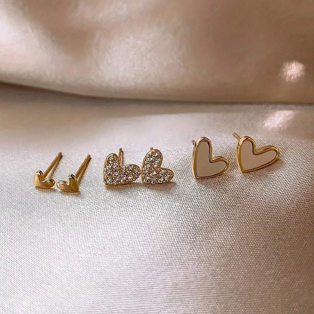 Three pairs of heart-shaped earrings in gold, black, black-white, and pink colours on display