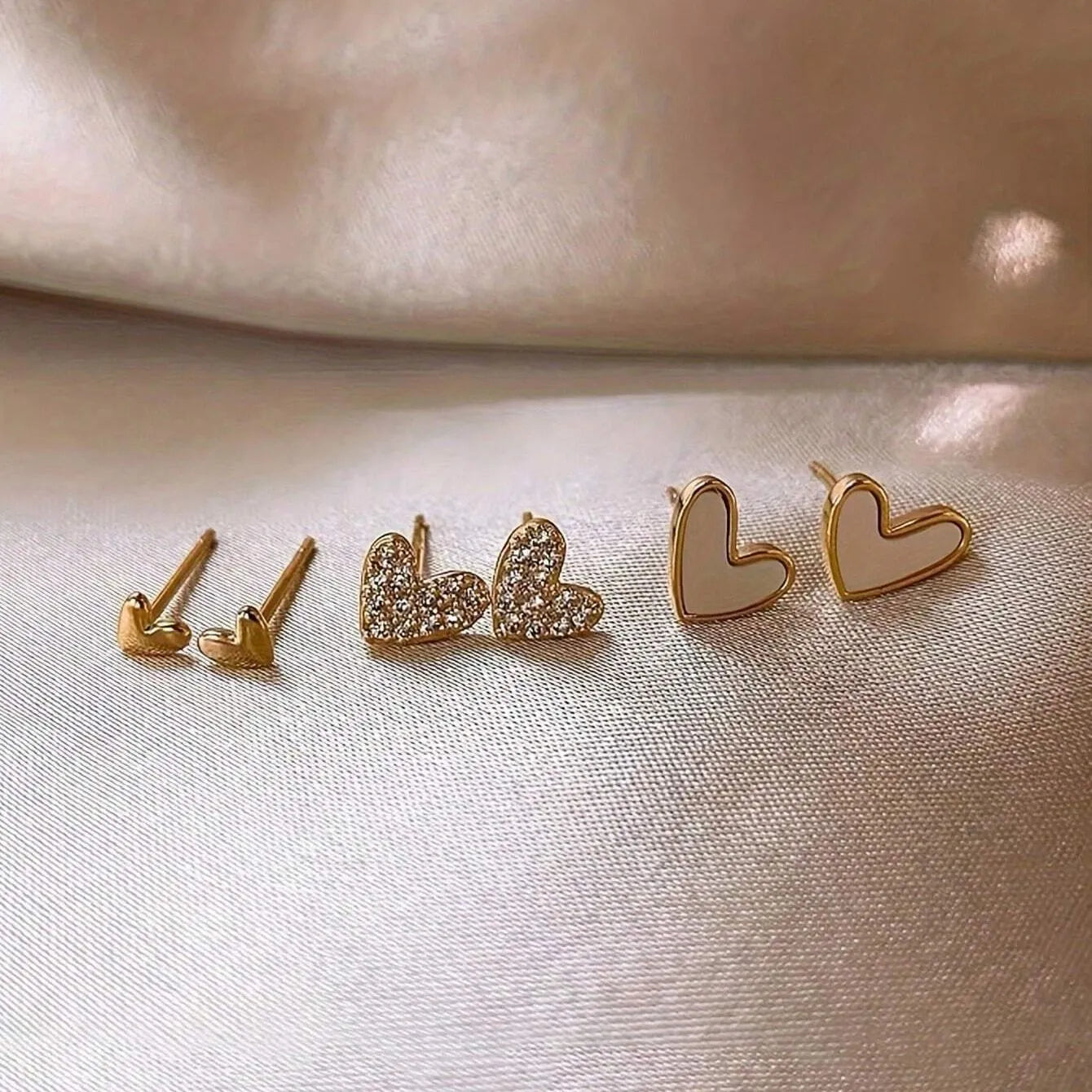 Three pairs of heart-shaped earrings in gold, black, black-white, and pink colours on display