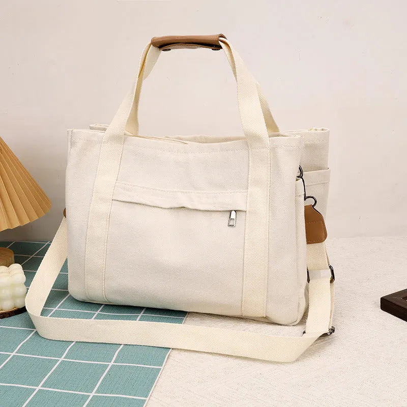 A horizontal square canvas tote bag in army green with a cross-body strap and visible sewing lines.