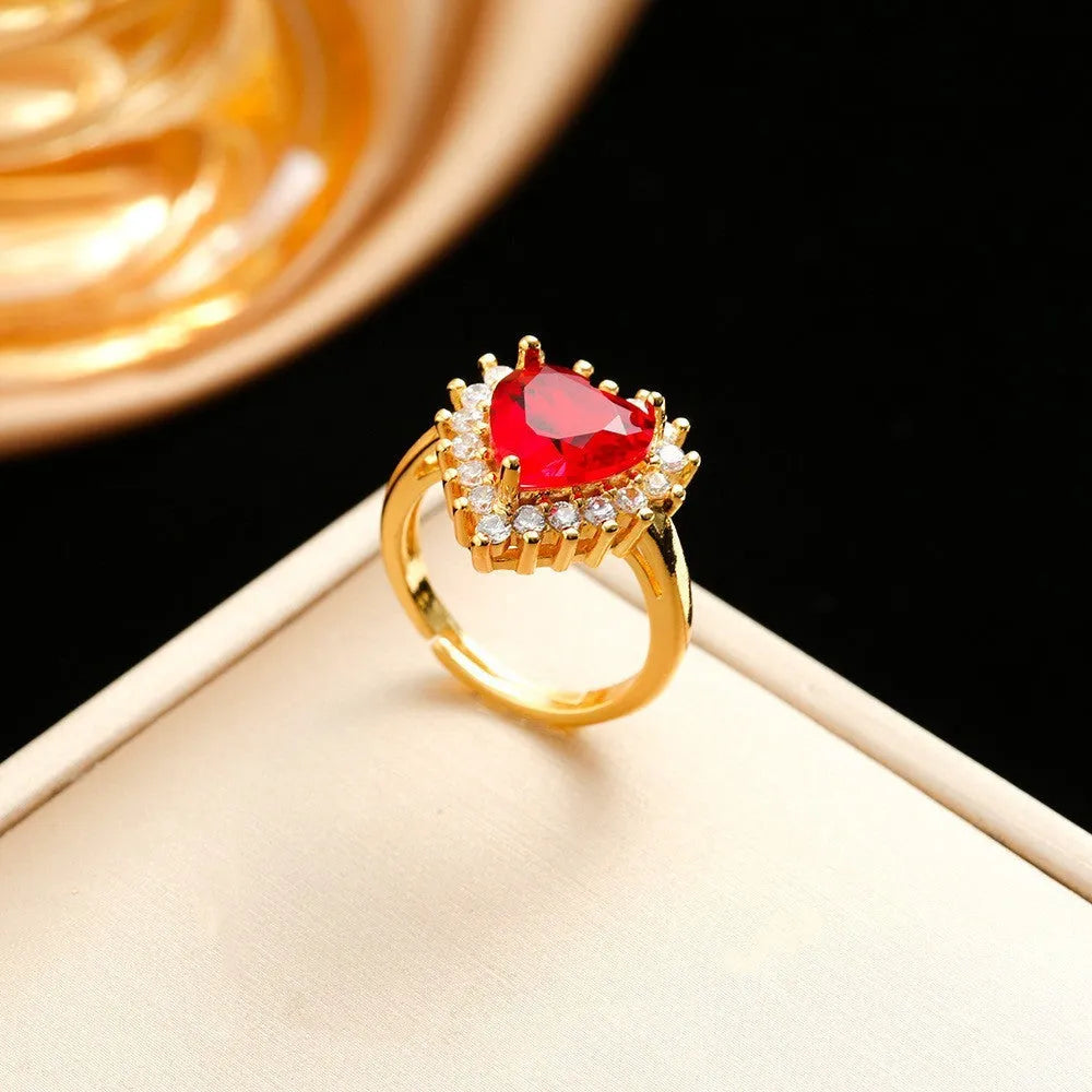 Gold-red titanium steel necklace with heart flower pendant, matching stud earrings, and ring on a grey background.